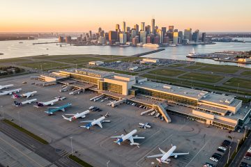 Vue aérienne réaliste de l’aéroport Boston Logan au lever du jour, avec des avions au sol, le port de Boston et la skyline en arrière-plan.