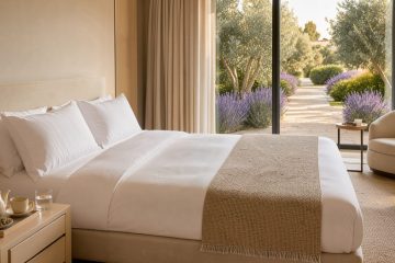 Suite d’hôtel de luxe lumineuse avec literie haut de gamme, plateau de tisane et vue sur un jardin méditerranéen.